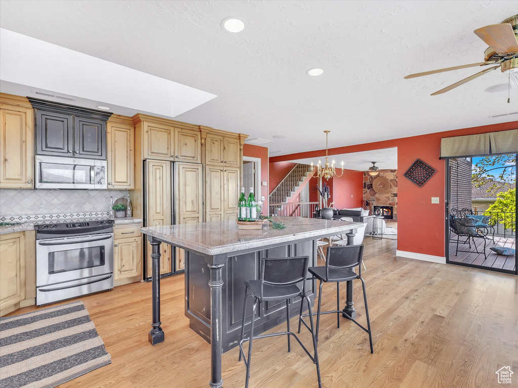 Kitchen with appliances with stainless steel finishes, a ceiling fan, a breakfast bar area, light wood-style flooring, and recessed lighting