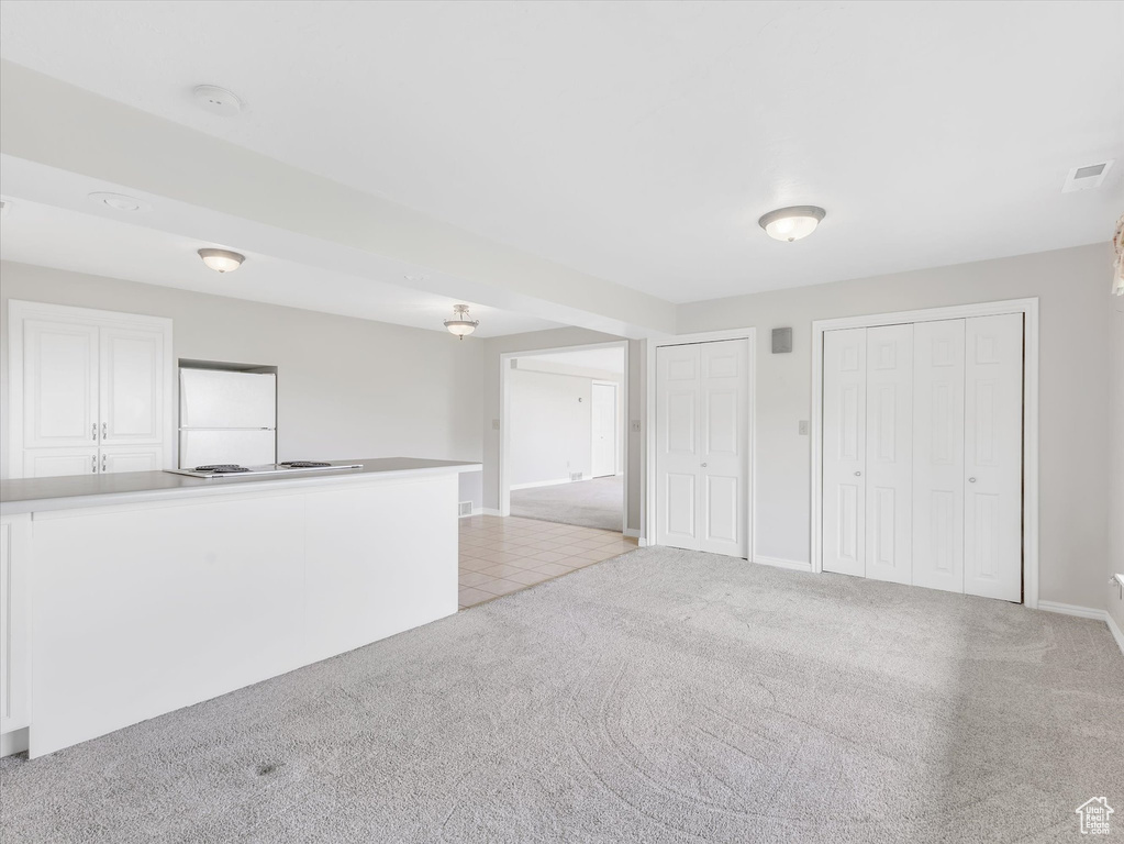 Unfurnished living room featuring light carpet and baseboards