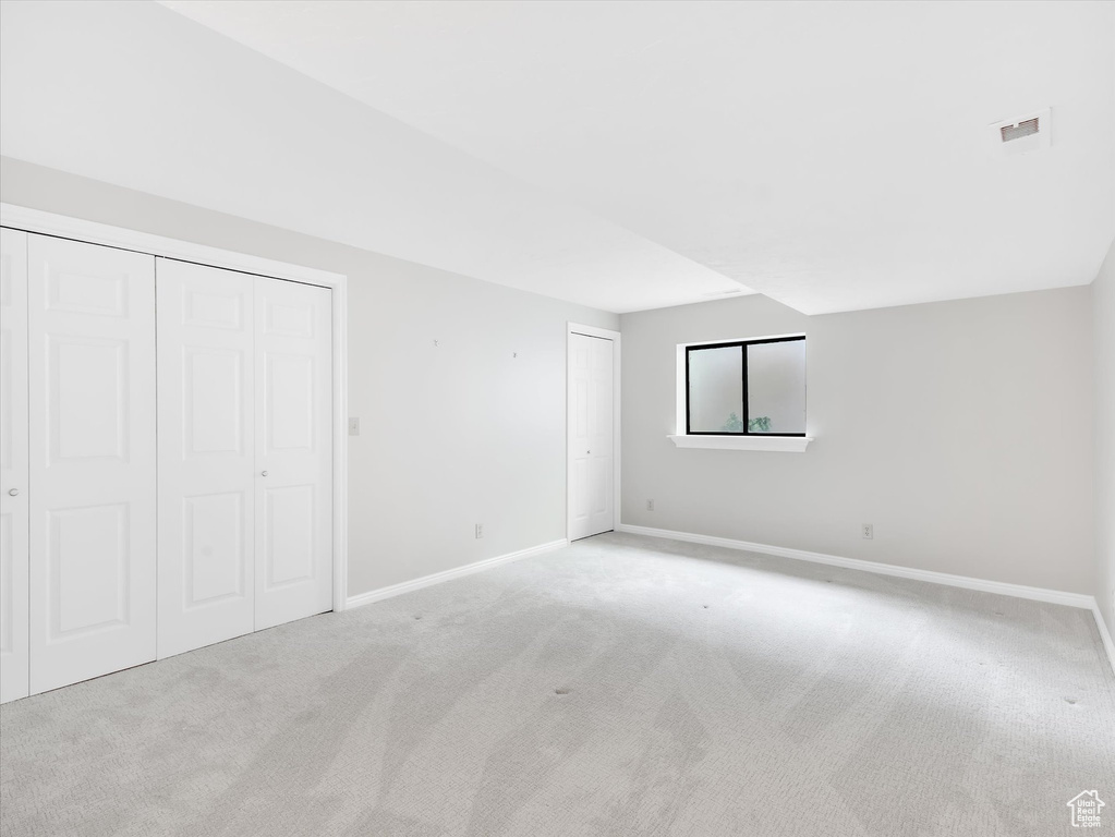 Unfurnished bedroom with light carpet, baseboards, and multiple closets