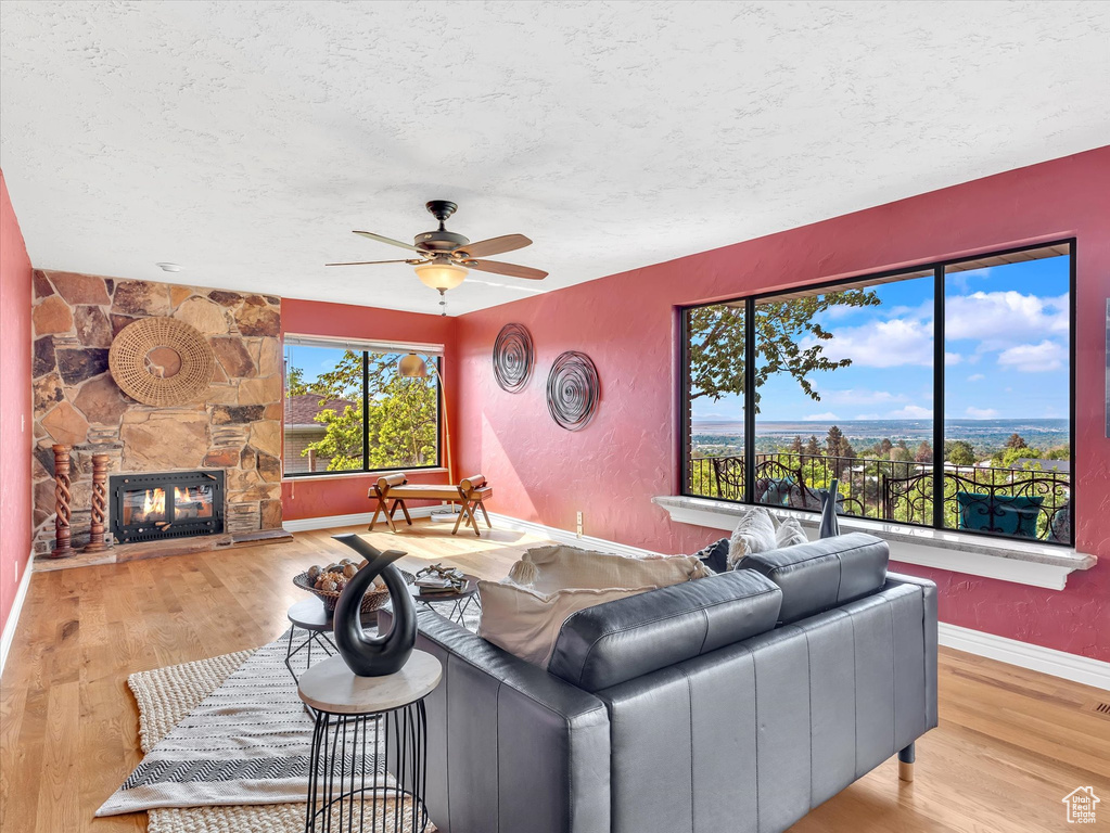 Living area with a ceiling fan, wood finished floors, a textured ceiling, a fireplace, and baseboards