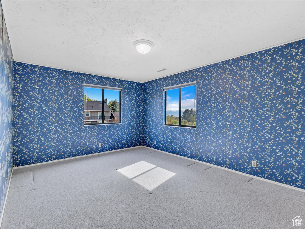 Carpeted empty room featuring wallpapered walls and a textured ceiling