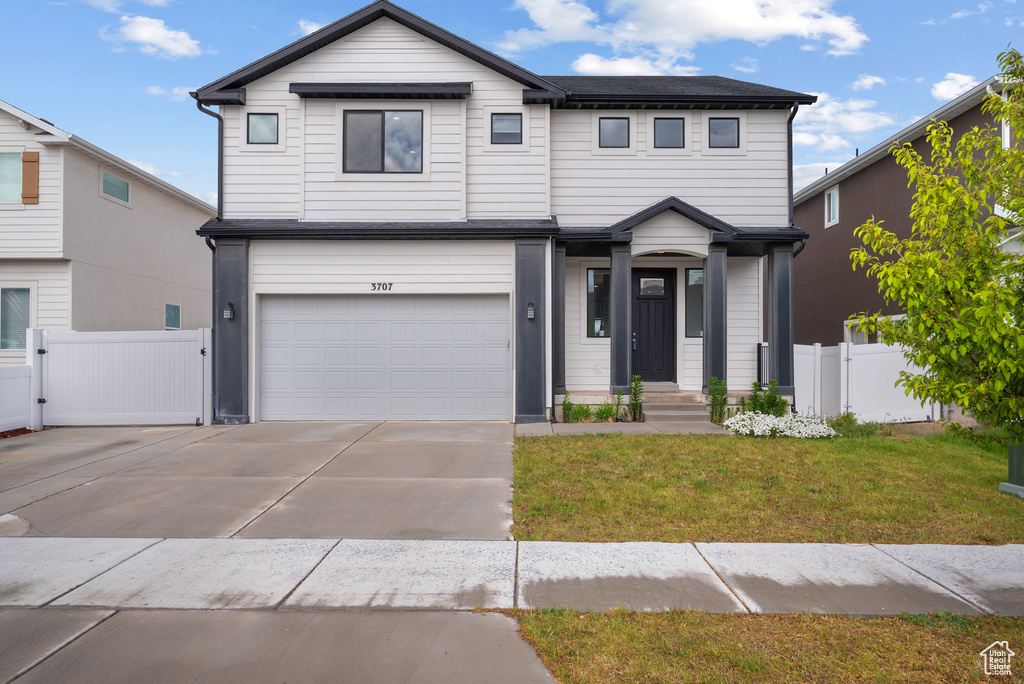 View of front of home with an attached garage, driveway, and a gate
