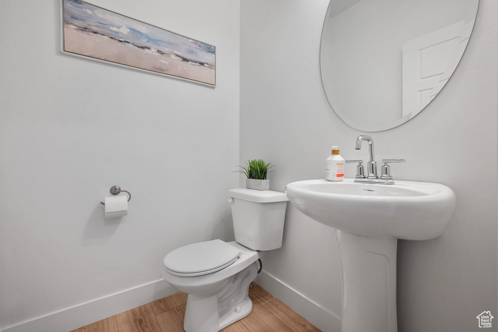 Half bathroom with baseboards, toilet, and wood finished floors