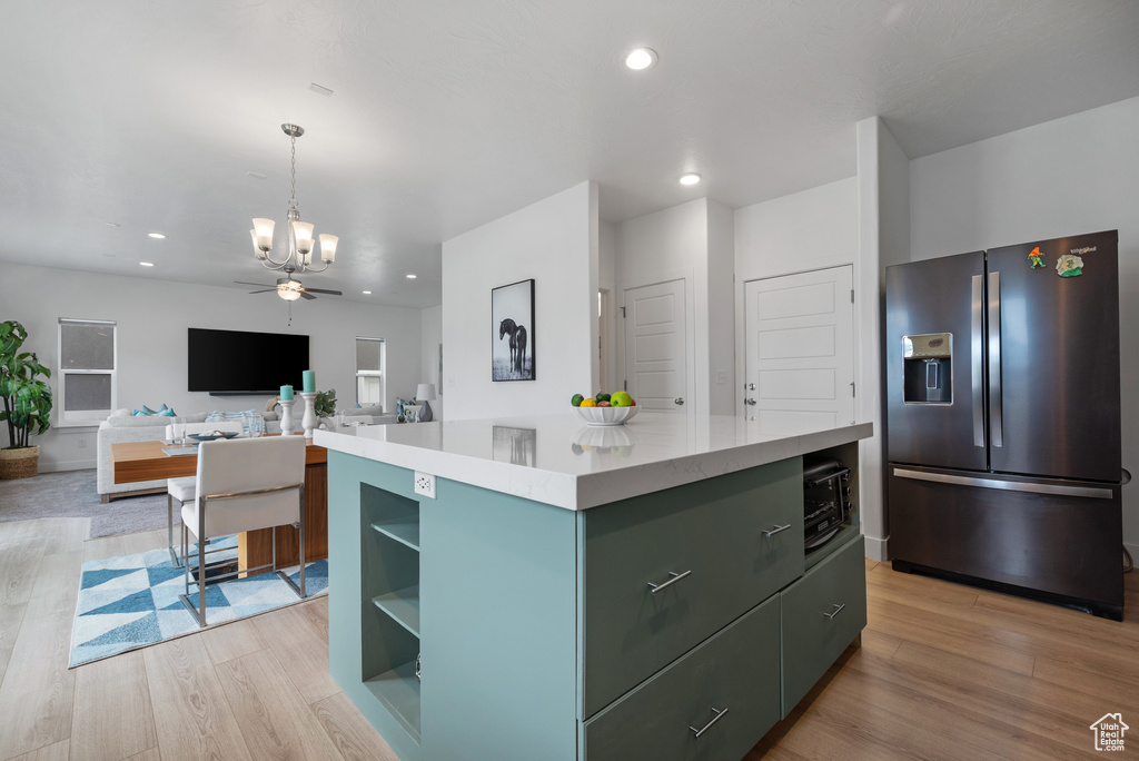 Kitchen featuring stainless steel fridge, light wood-style flooring, a chandelier, a center island, and light countertops