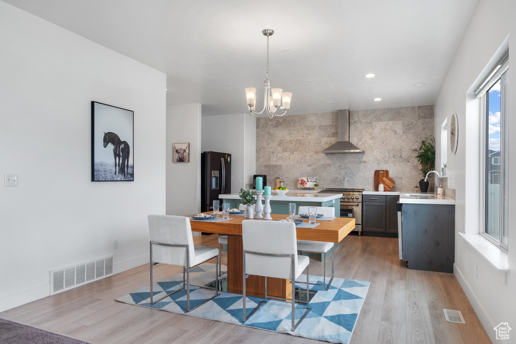 Kitchen featuring wall chimney range hood, high end stove, a sink, light countertops, and black fridge with ice dispenser