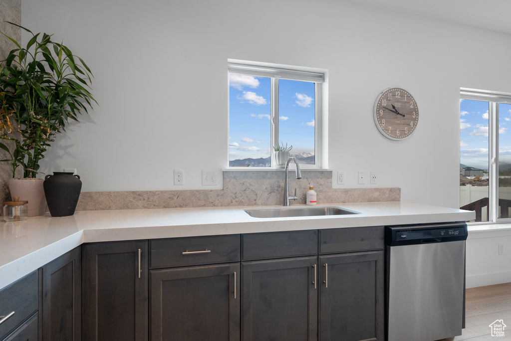Kitchen featuring stainless steel dishwasher, a sink, light countertops, and light wood-style floors
