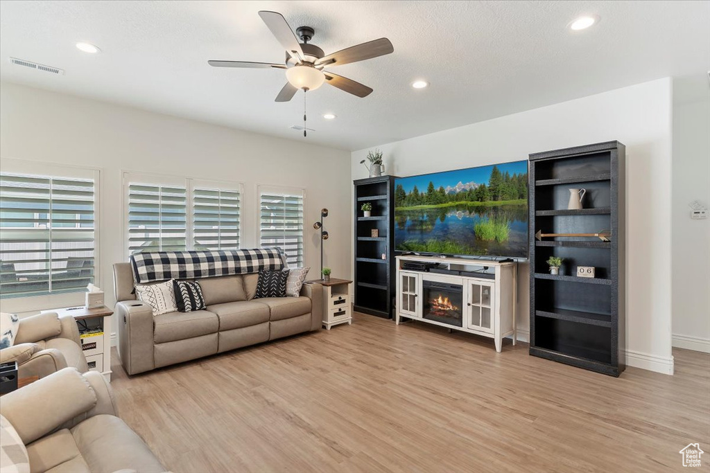 Living area featuring wood finished floors, a ceiling fan, recessed lighting, a warm lit fireplace, and baseboards