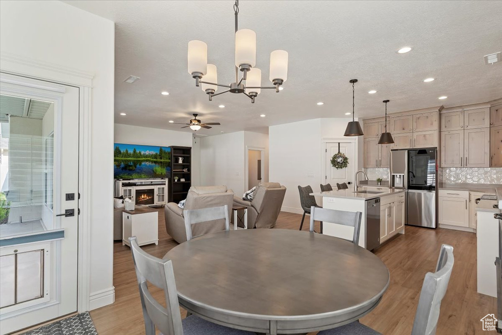 Dining space with ceiling fan, a chandelier, wood finished floors, recessed lighting, and a warm lit fireplace