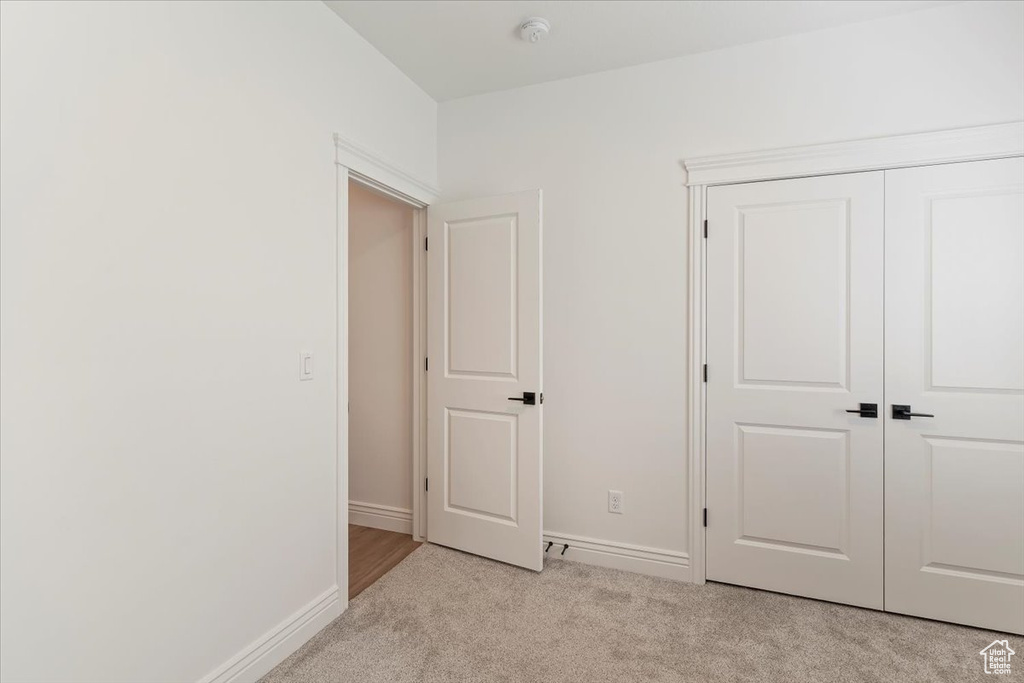 Unfurnished bedroom featuring light carpet, baseboards, and a closet