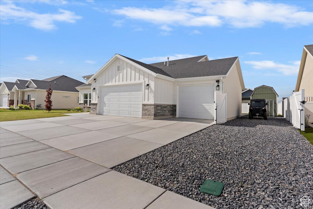 View of side of property with board and batten siding, an attached garage, driveway, fence, and stone siding