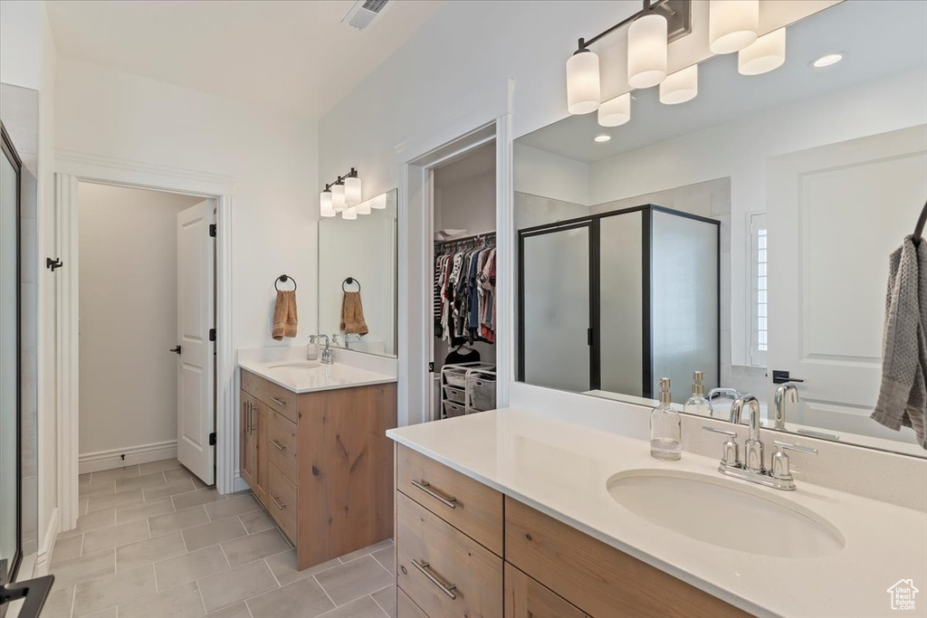 Bathroom featuring a shower stall, two vanities, a spacious closet, tile patterned flooring, and baseboards
