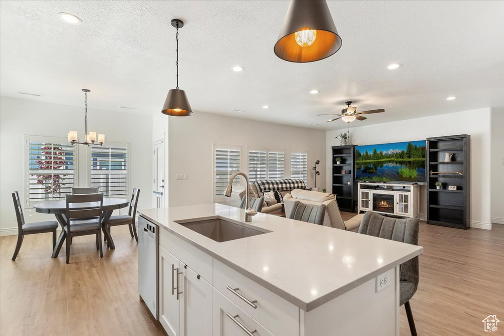 Kitchen with a sink, light countertops, ceiling fan, light wood-style floors, and a chandelier