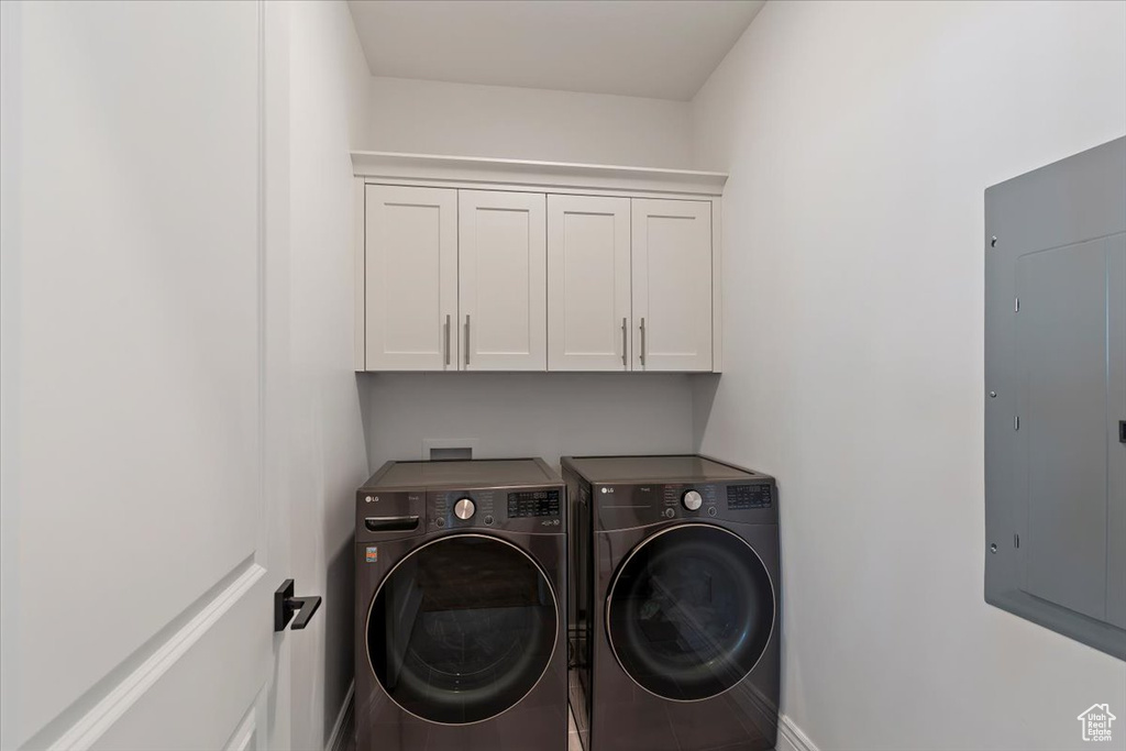 Laundry area featuring washing machine and clothes dryer, electric panel, cabinet space, and baseboards