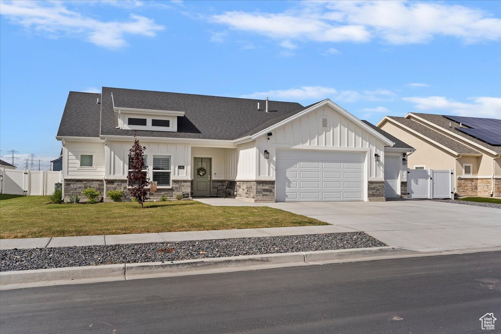 View of front of property featuring a gate, stone siding, board and batten siding, an attached garage, and driveway