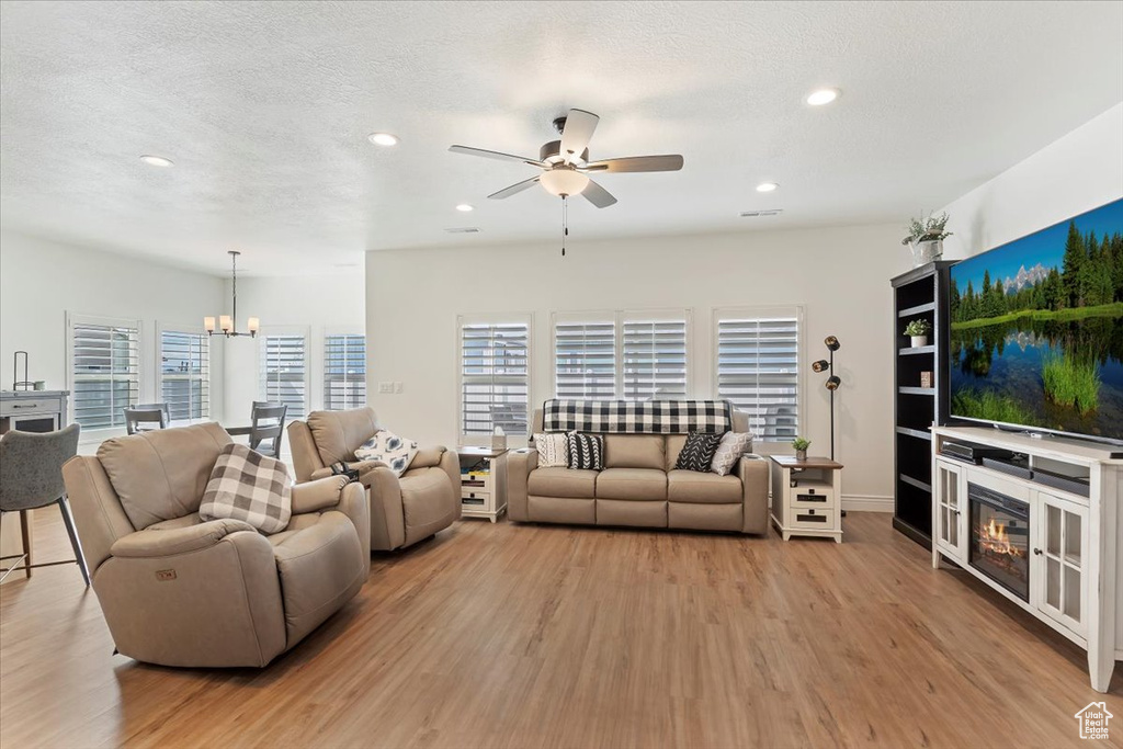 Living area featuring light wood-style floors, ceiling fan, recessed lighting, a chandelier, and a glass covered fireplace