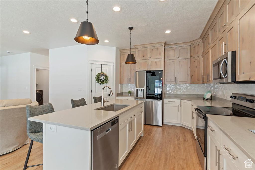 Kitchen featuring appliances with stainless steel finishes, a sink, a kitchen breakfast bar, light wood finished floors, and open floor plan