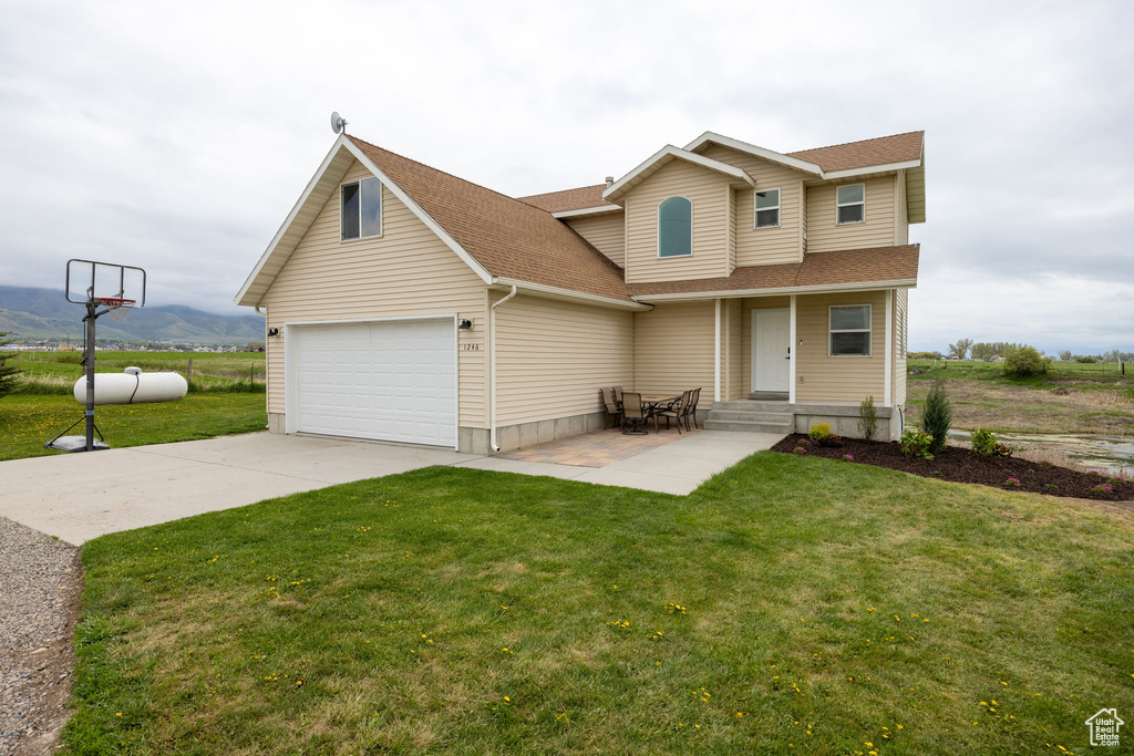 View of front of property with a shingled roof, concrete driveway, a front lawn, and a mountain view
