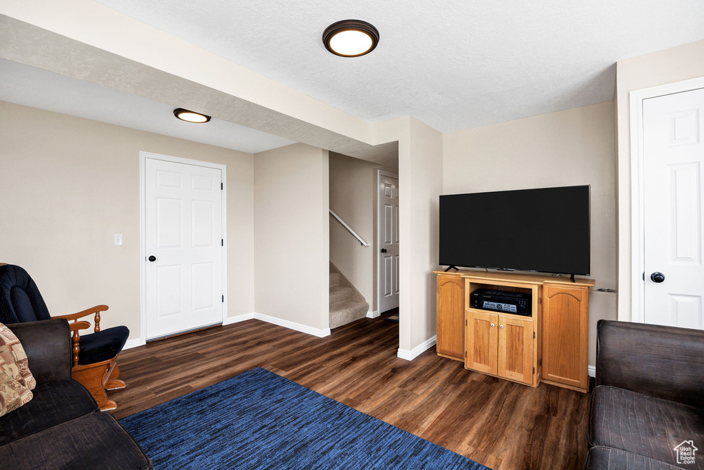Living room featuring dark wood-style flooring, stairs, and baseboards