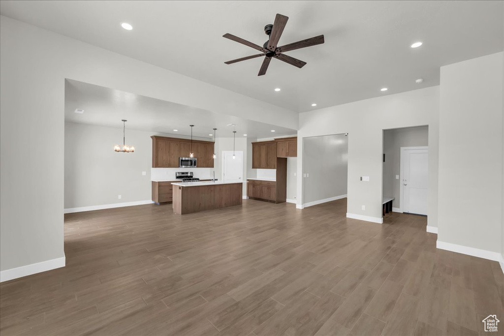 Unfurnished living room featuring ceiling fan, dark wood-style flooring, a chandelier, baseboards, and recessed lighting