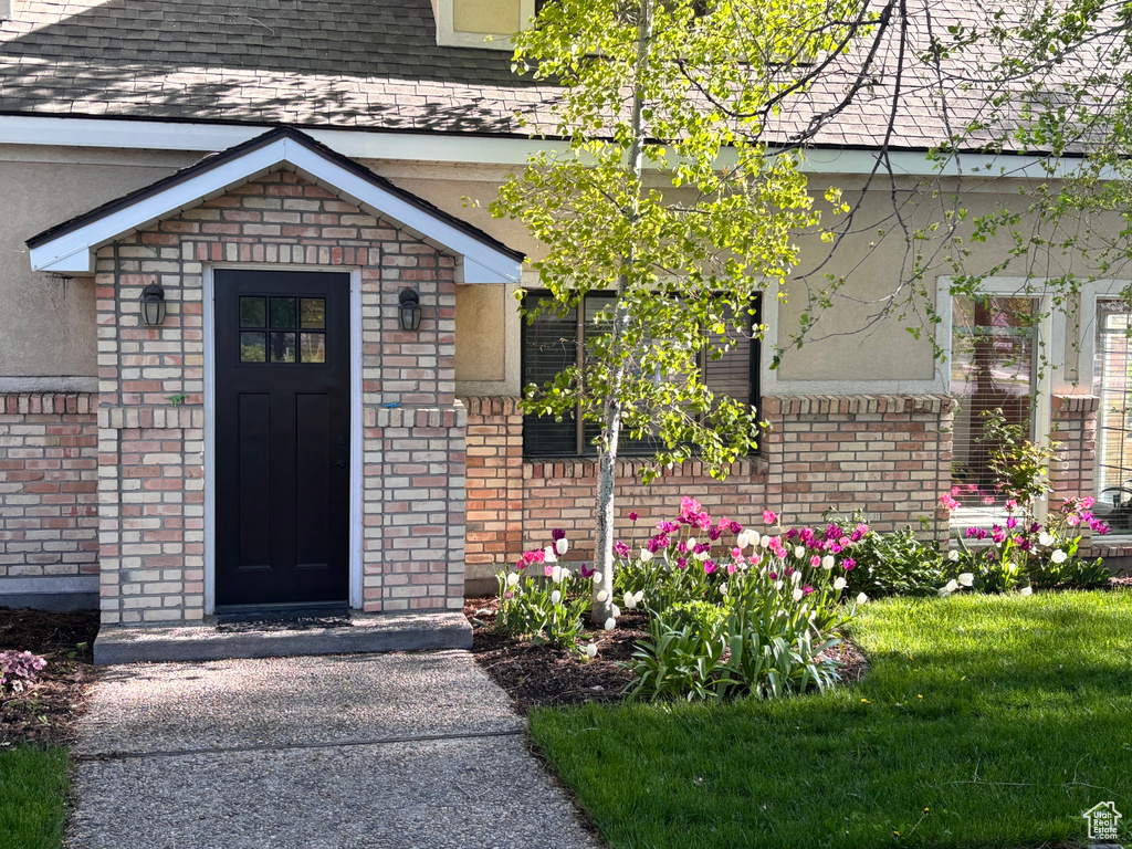 Entrance to property featuring roof with shingles, brick siding, and stucco siding