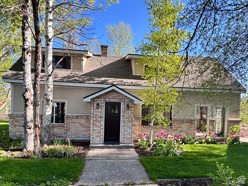 View of front of home featuring a front yard, stucco siding, a chimney, and a shingled roof