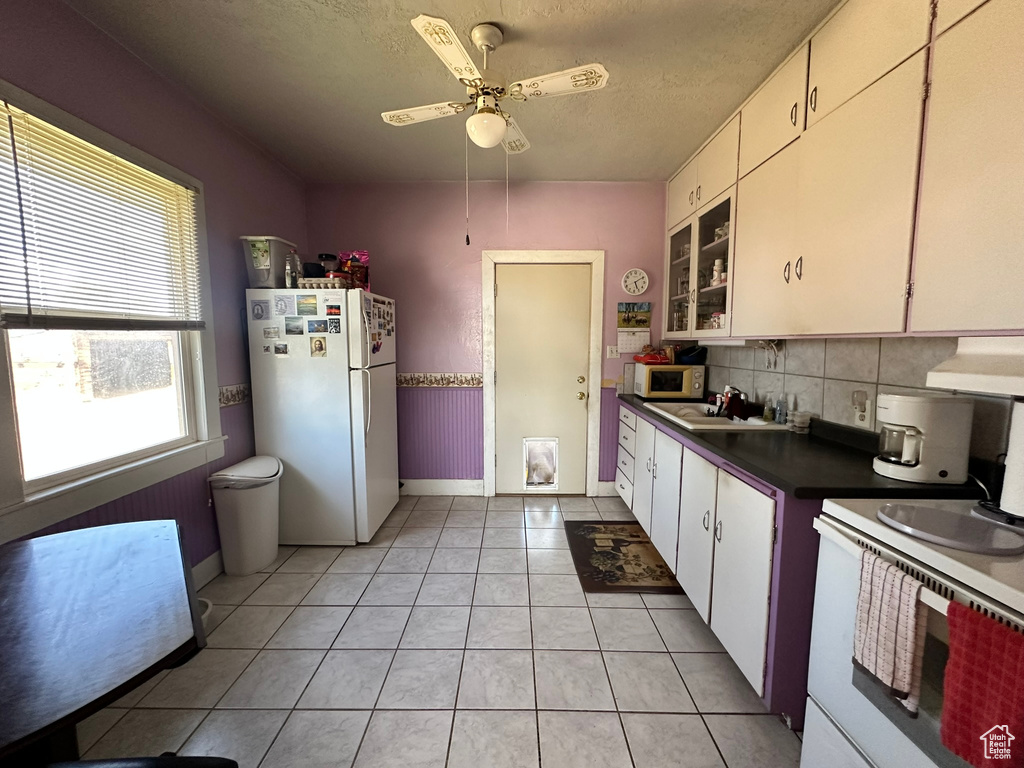 Kitchen featuring white appliances, dark countertops, baseboards, light tile patterned floors, and backsplash