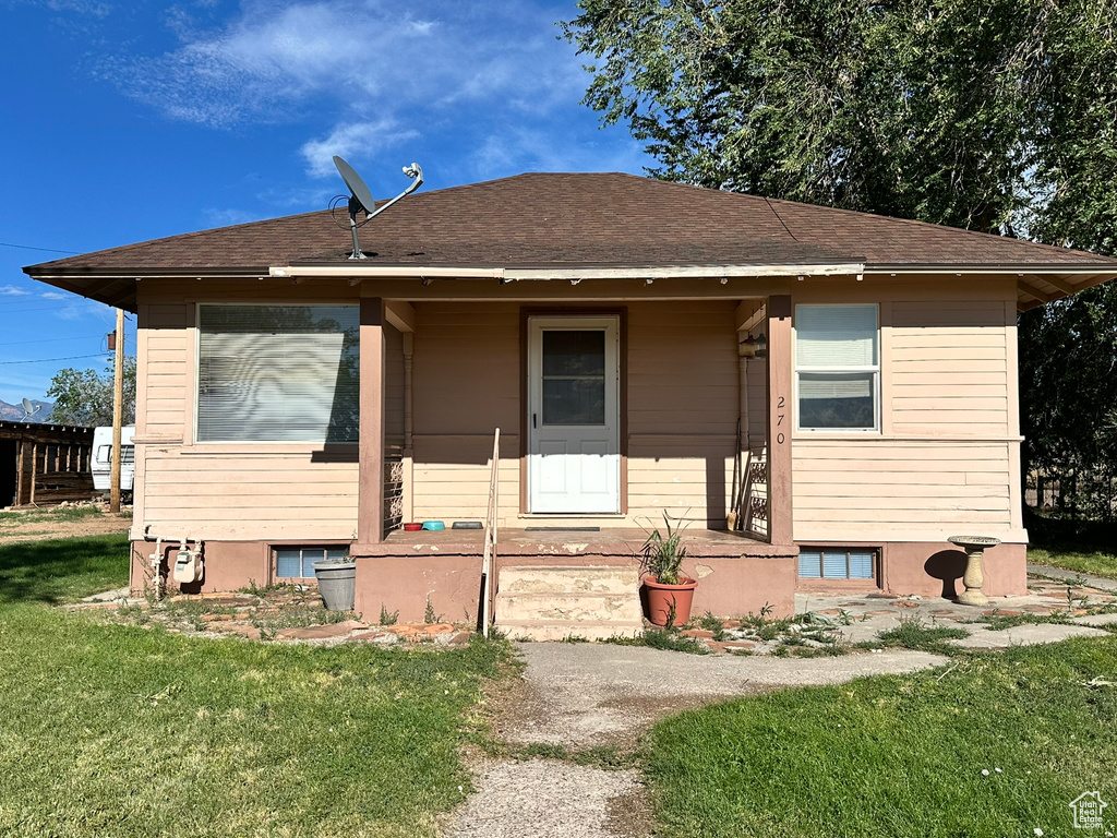 Bungalow-style home with a front yard, a shingled roof, and a porch