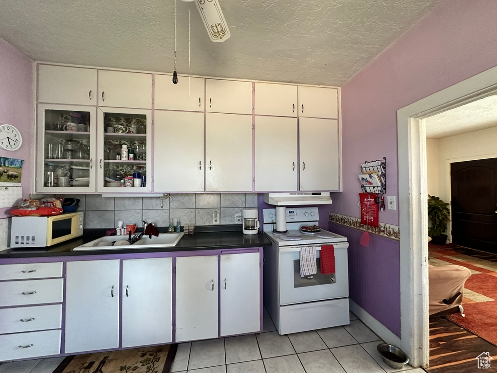 Kitchen with white appliances, a textured ceiling, dark countertops, white cabinetry, and under cabinet range hood