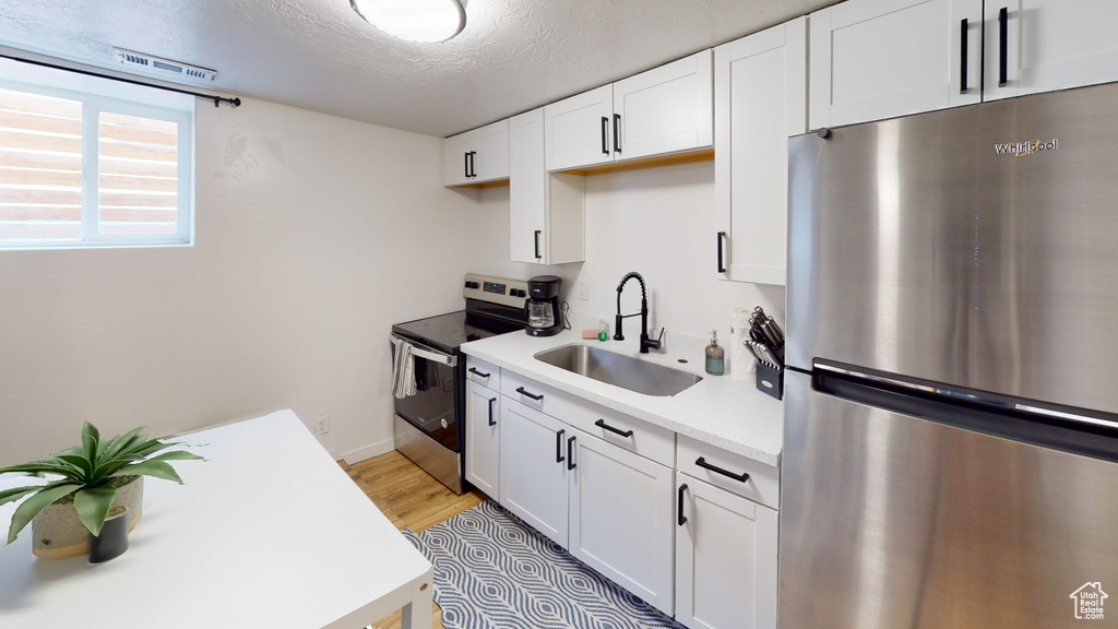 Kitchen featuring stainless steel appliances, a sink, light countertops, white cabinets, and a textured ceiling
