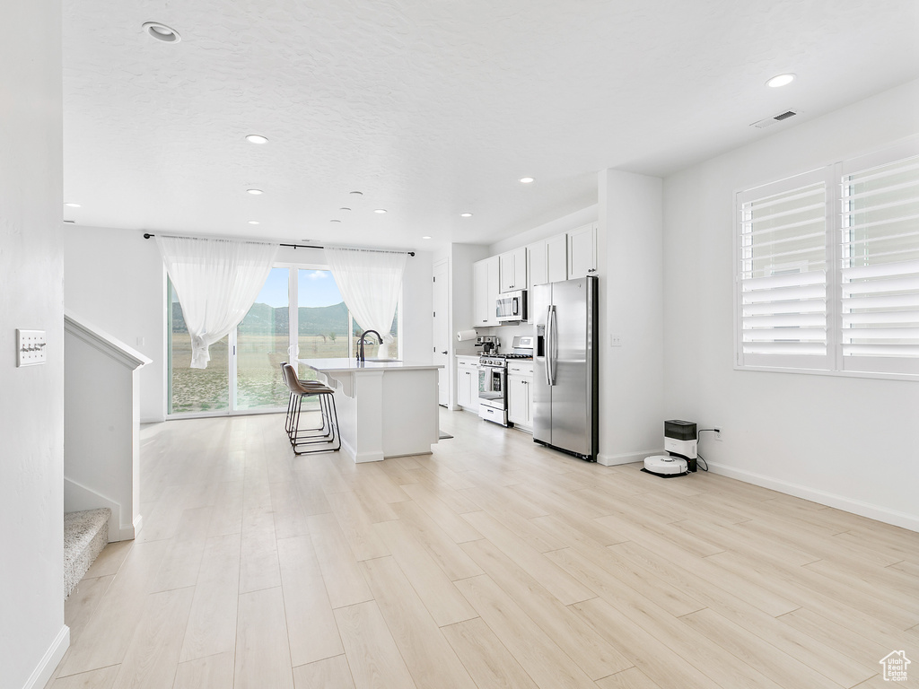 Kitchen with appliances with stainless steel finishes, white cabinets, light wood-style flooring, a breakfast bar, and recessed lighting