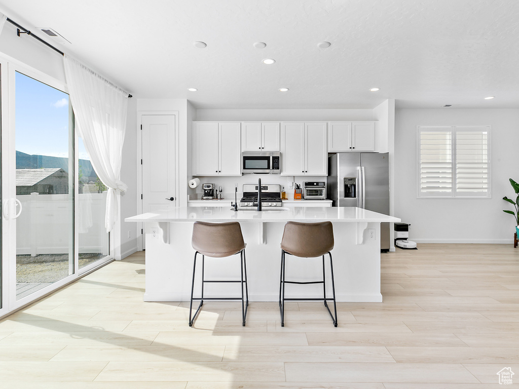 Kitchen with appliances with stainless steel finishes, recessed lighting, light countertops, a kitchen island with sink, and white cabinetry