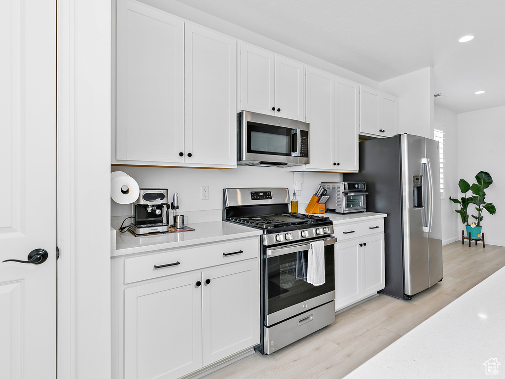 Kitchen with appliances with stainless steel finishes, light countertops, light wood-style floors, white cabinets, and recessed lighting