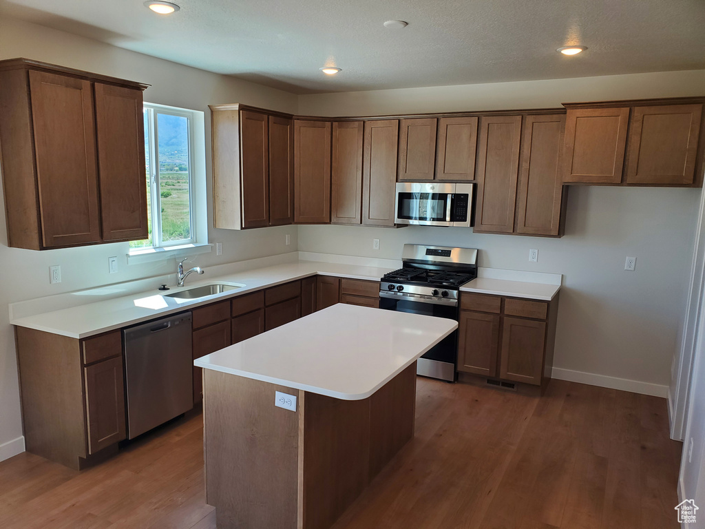 Kitchen featuring stainless steel appliances, wood finished floors, a sink, baseboards, and light countertops