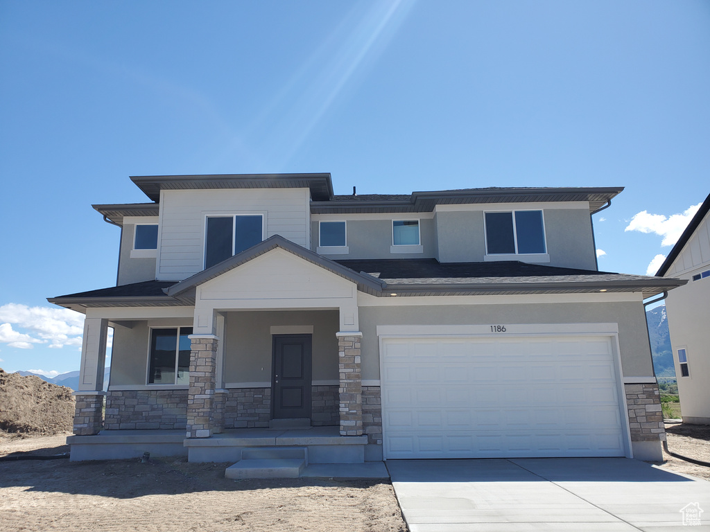 View of front of house featuring stone siding, an attached garage, driveway, covered porch, and stucco siding