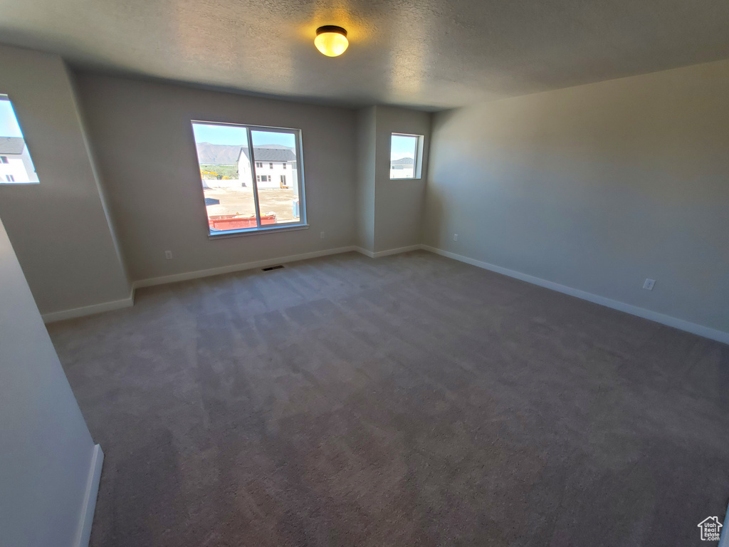 Unfurnished room with baseboards, a textured ceiling, and dark colored carpet
