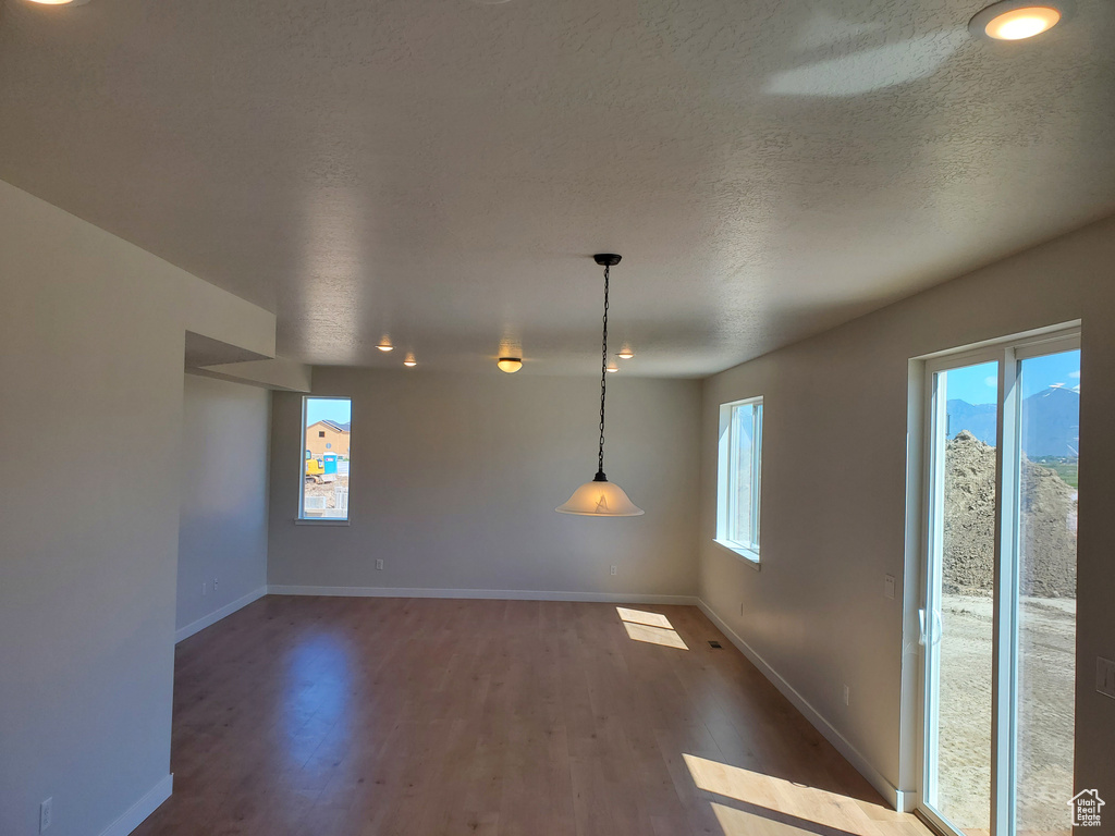Unfurnished dining area with wood finished floors, baseboards, a textured ceiling, and recessed lighting