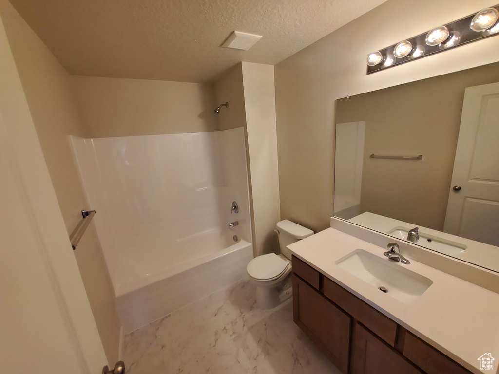 Bathroom with marble finish floors, a textured ceiling, toilet, vanity, and bathing tub / shower combination