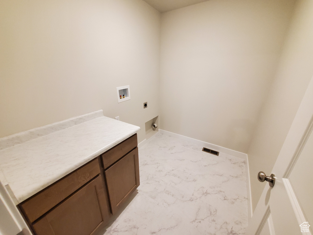 Clothes washing area featuring hookup for an electric dryer, washer hookup, cabinet space, light marble finish floors, and baseboards