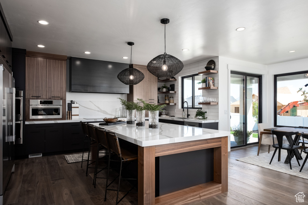 Kitchen with open shelves, appliances with stainless steel finishes, a sink, a center island, and a kitchen breakfast bar