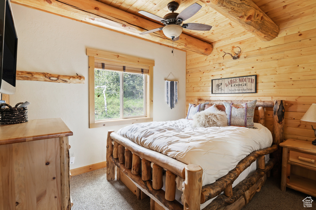 Bedroom with wood ceiling with exposed beams, light colored carpet, baseboards, and wood walls