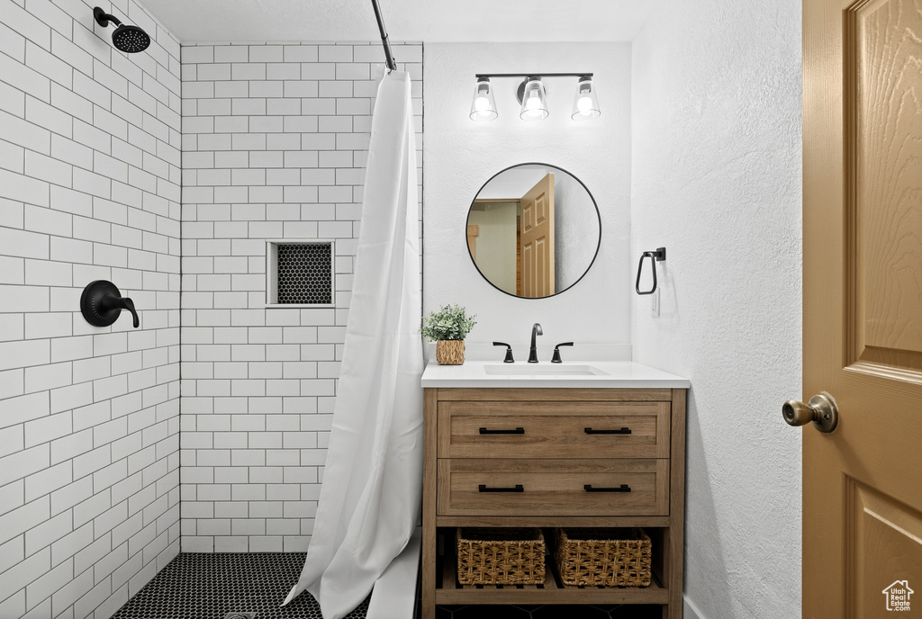 Full bath featuring tiled shower, vanity, and a textured wall
