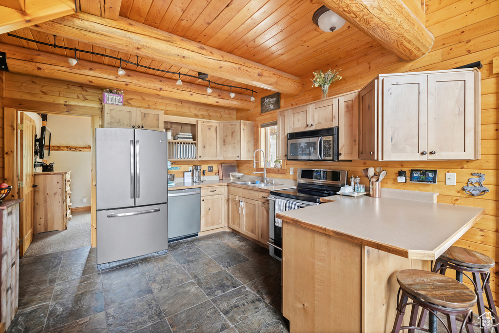 Kitchen with appliances with stainless steel finishes, a sink, wooden ceiling with exposed beams, a peninsula, and dark stone finish floors