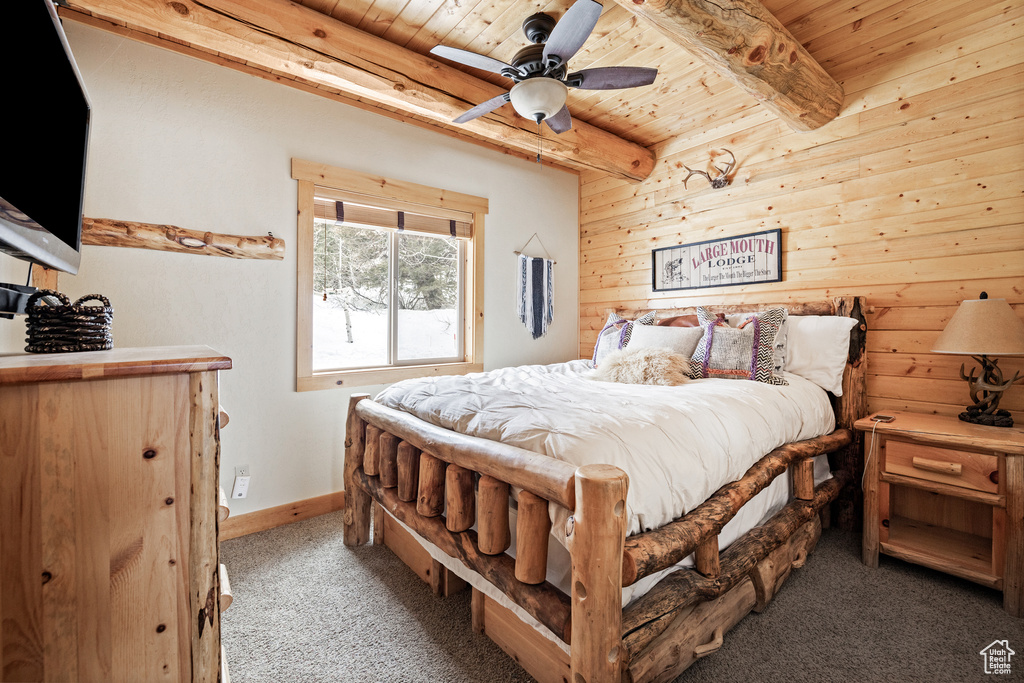 Carpeted bedroom with wooden ceiling, beam ceiling, wooden walls, baseboards, and ceiling fan