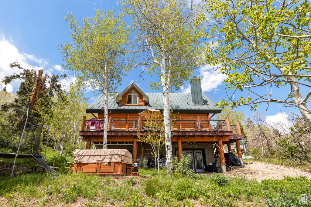 Rear view of property with a hot tub, a deck, metal roof, a chimney, and log siding