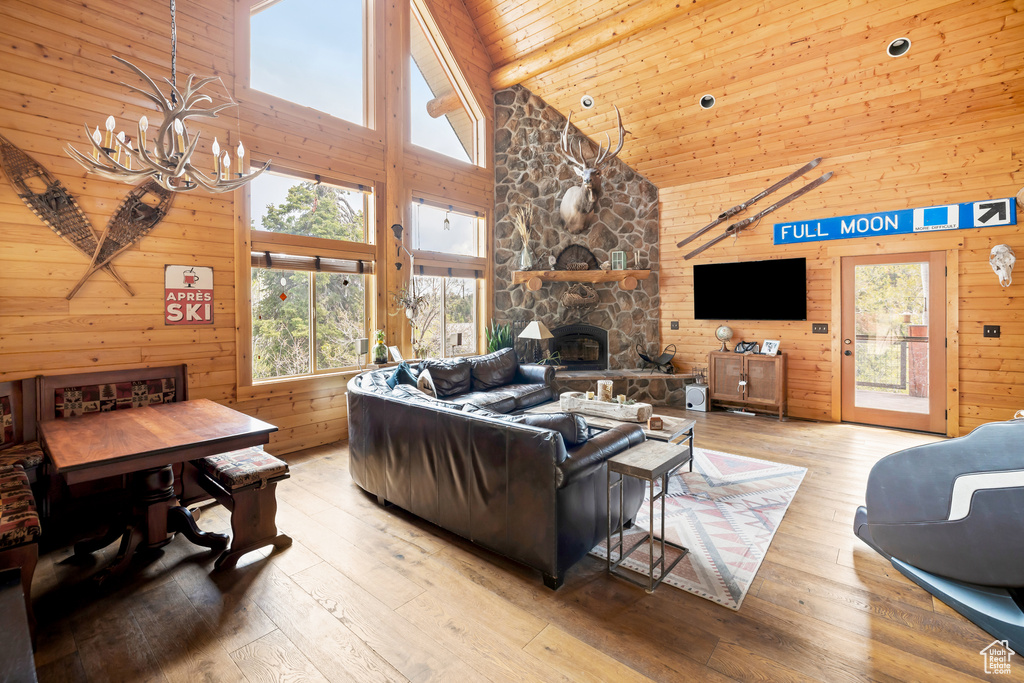 Living area with a chandelier, high vaulted ceiling, wooden walls, a stone fireplace, and light wood-style floors