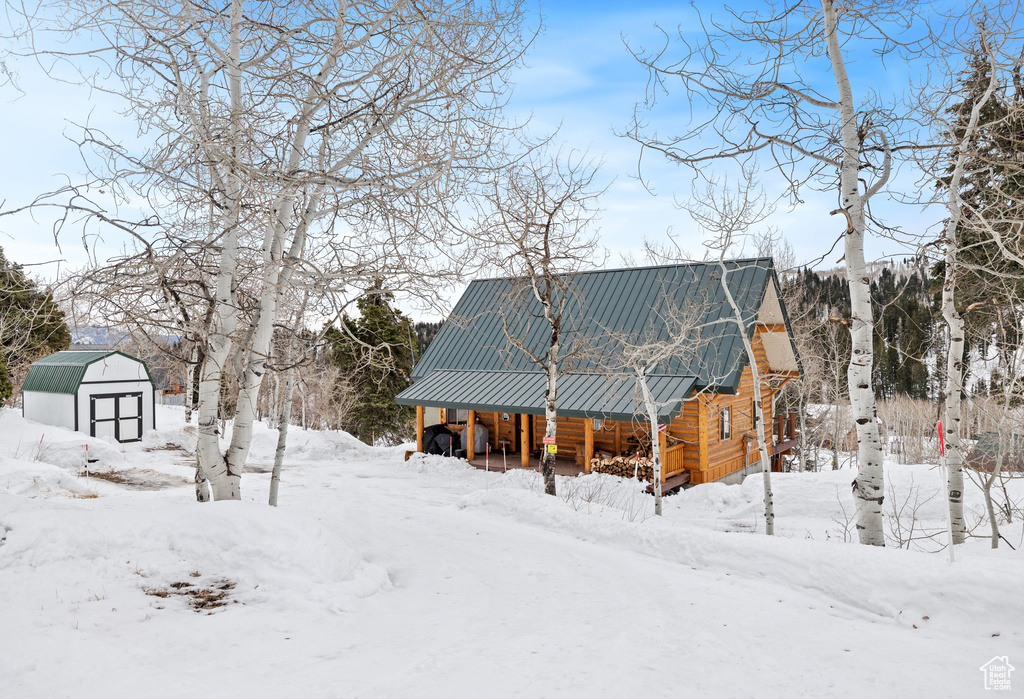 Snow covered property featuring metal roof, a storage unit, and an outbuilding