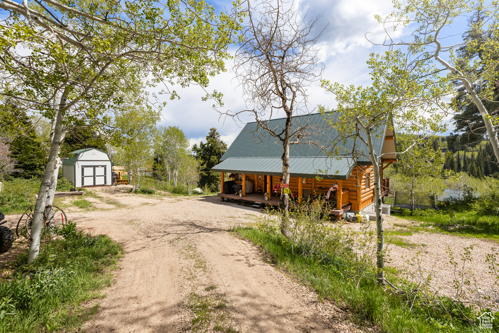 View of front of house featuring a porch, dirt driveway, metal roof, and log siding
