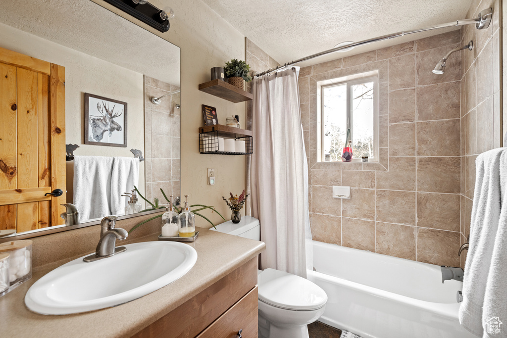 Bathroom with a textured ceiling, shower / tub combo, toilet, and vanity