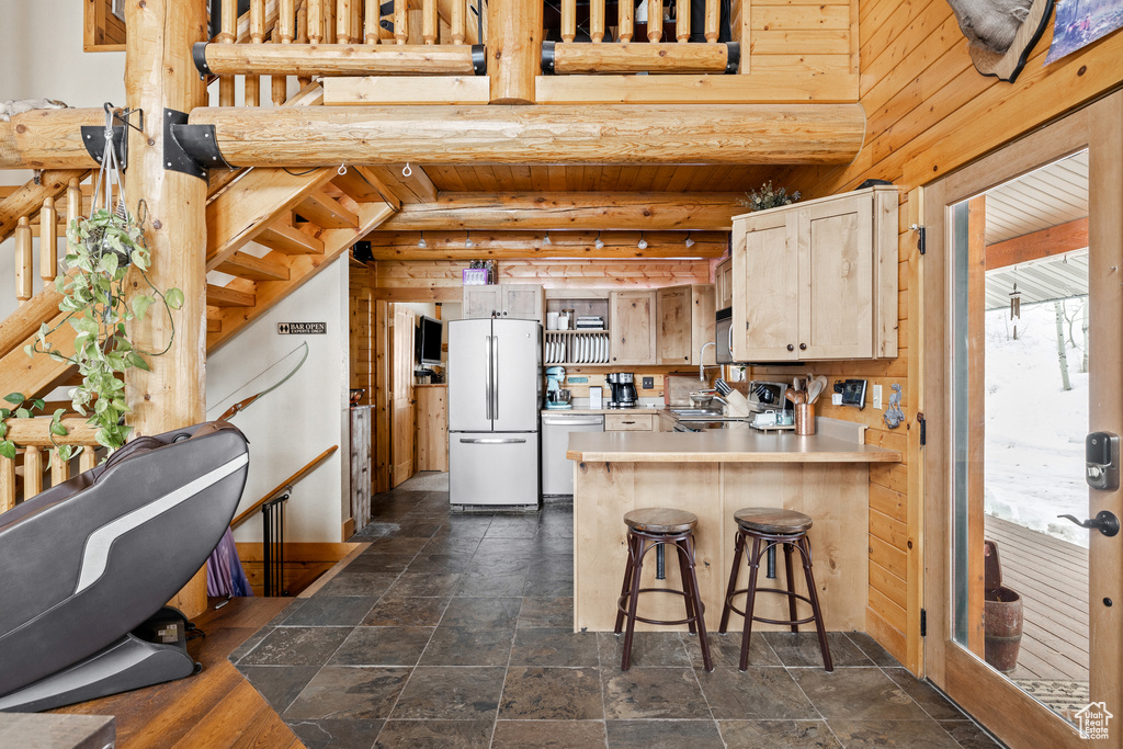 Kitchen with freestanding refrigerator, dishwasher, a peninsula, light countertops, and dark stone finish floors