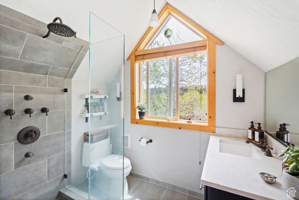 Bathroom with lofted ceiling, a tile shower, vanity, toilet, and baseboards